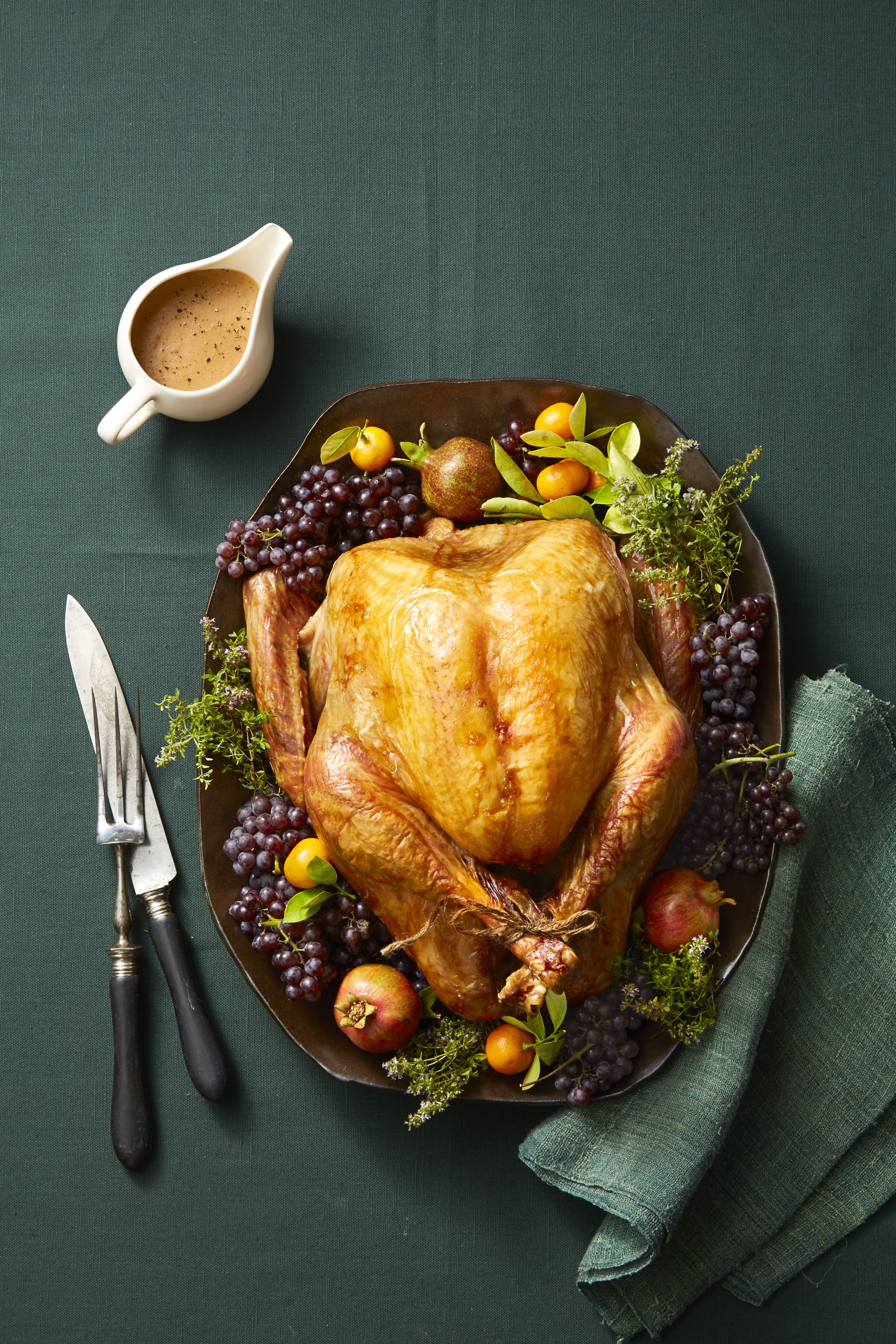 https://hips.hearstapps.com/hmg-prod/images/whole-roast-turkey-on-platter-with-garnishes-and-green-tablecoth-1599755530.jpg