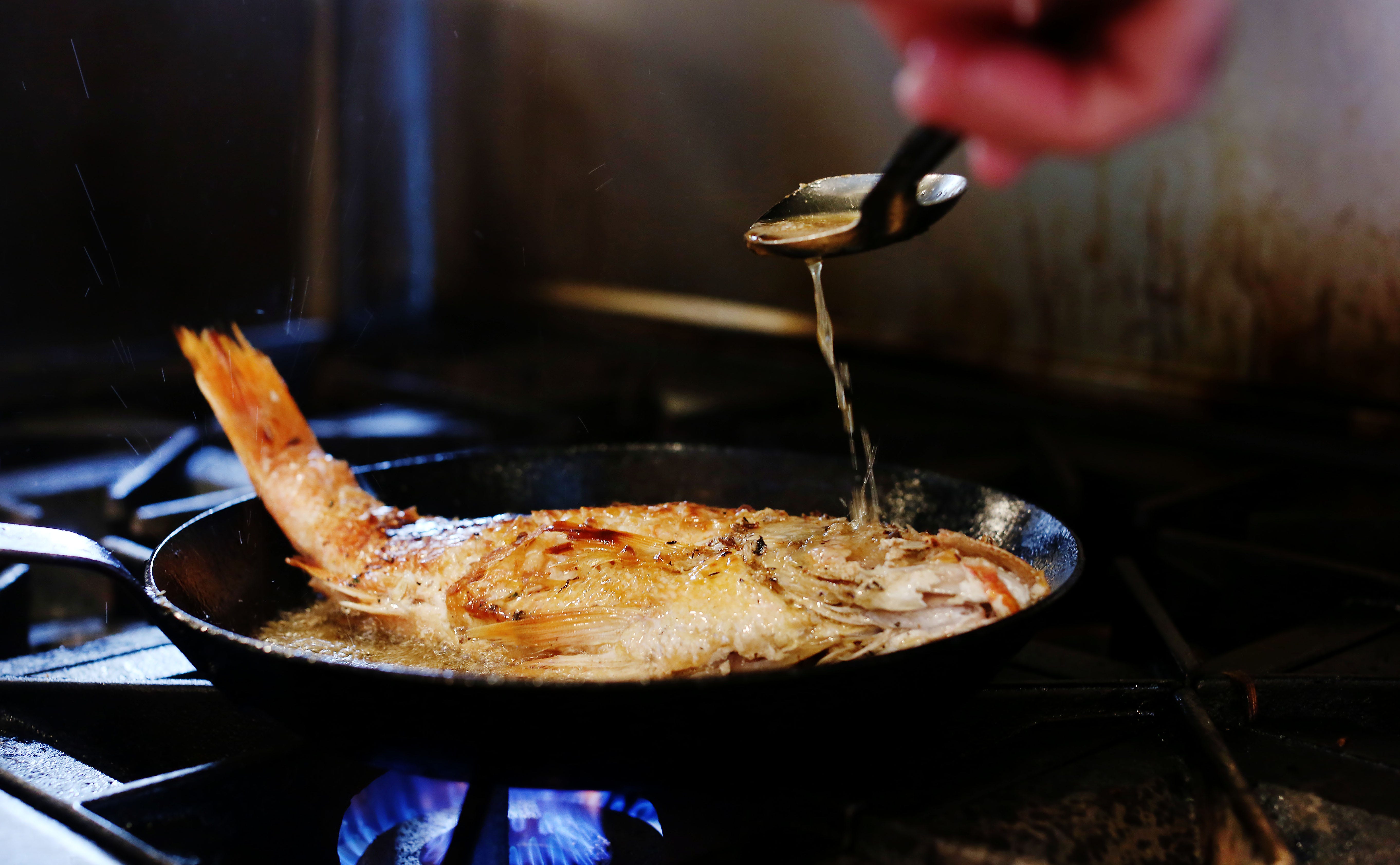 whole snapper being sauteed in a pan