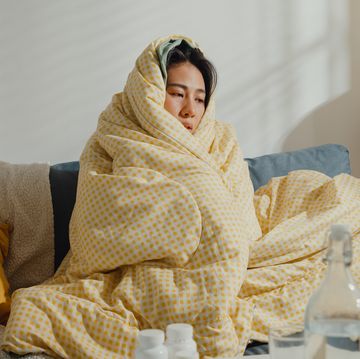 sick woman sneezing as she sits under blanket