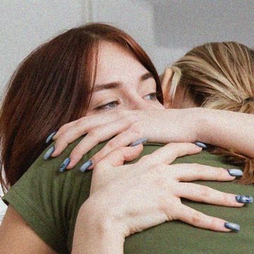 a girl looking sad hugging her friend whose face is obscured