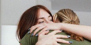 a girl looking sad hugging her friend whose face is obscured