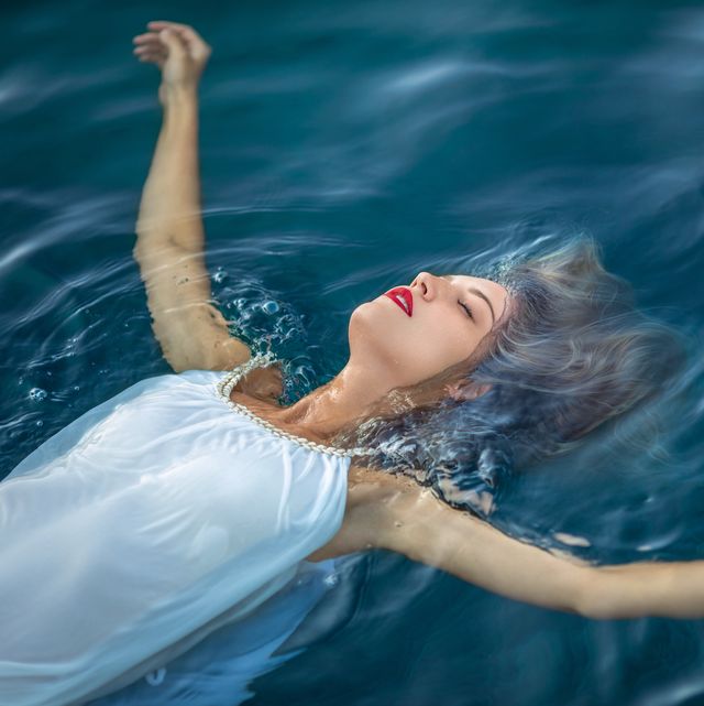 young woman with long blonde hair wearing white dress and floating on water surface