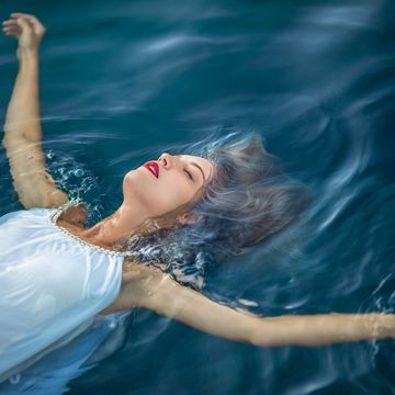 young woman with long blonde hair wearing white dress and floating on water surface