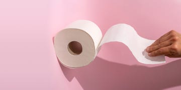 cropped hand holding a toilet roll on pink background