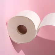cropped hand holding a toilet roll on pink background
