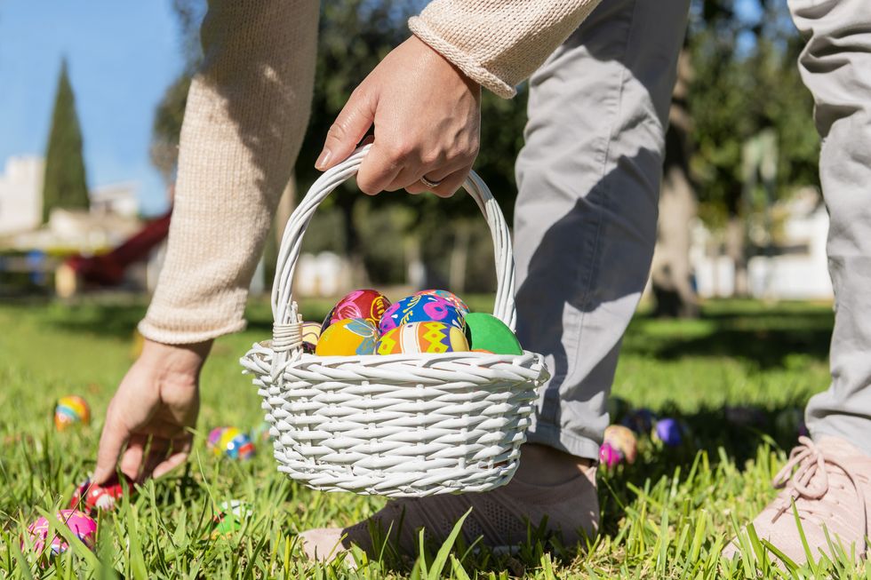 close up of female holding an easter egg basket and hiding eggs in the grass on an out of focus background selective focus easter concept
