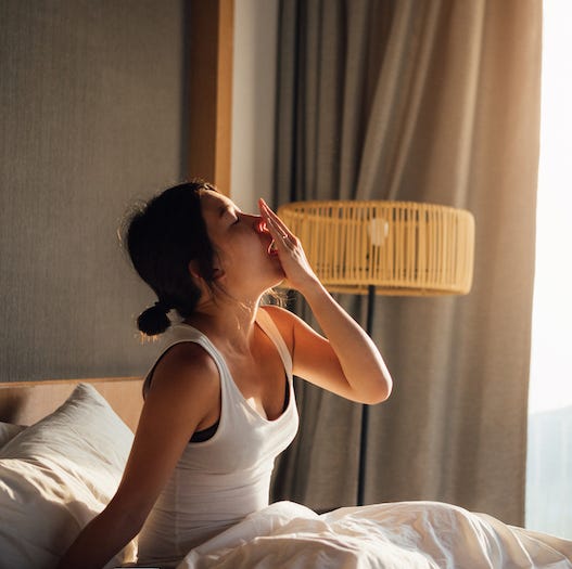 beautiful young asian woman covering her mouth with one hand while yawning, waking up in bed in the morning