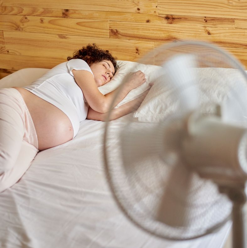pregnant woman lying in bed has difficulty sleeping due to heat wave, she uses an electric fan in her bedroom