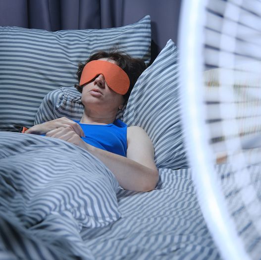 woman in bed sleeping with a fan in the foreground