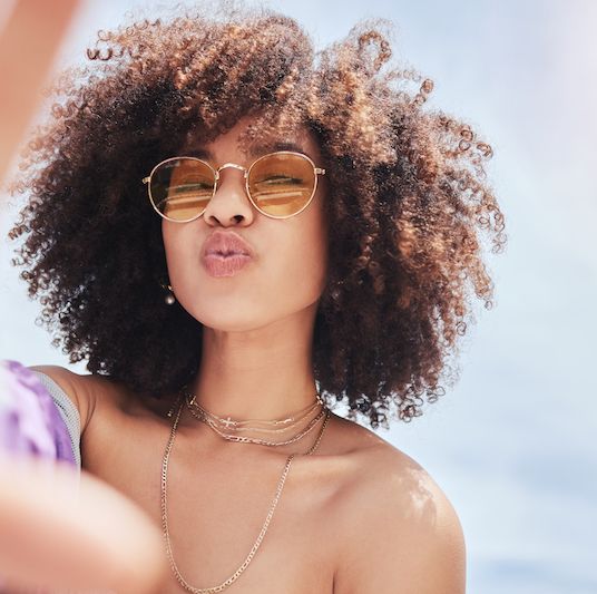portrait of young trendy beautiful mixed race woman with an afro smiling and posing for a selfie while wearing sunglasses