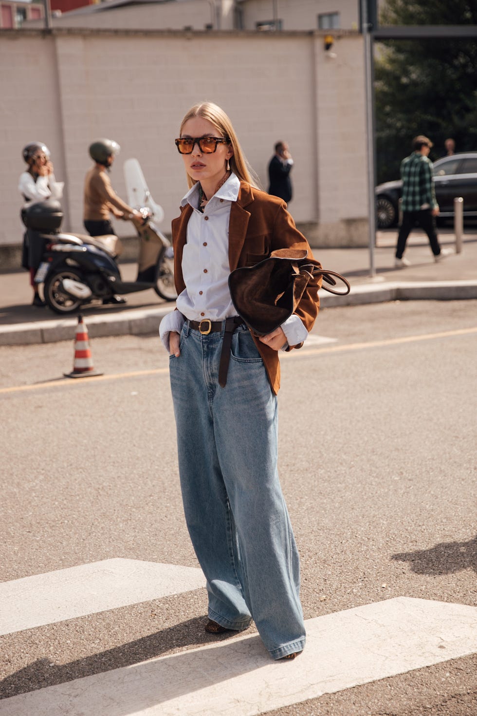 a woman wears wide leg jeans and brown suede accessories during fashion week