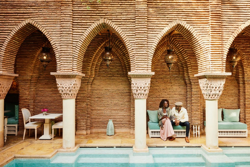 wide shot of couple holding hands while sitting in courtyard of luxury hotel
