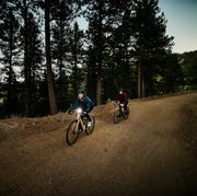 daylight savings cycling wide shot of female athletes on night gravel bike ride on forest road