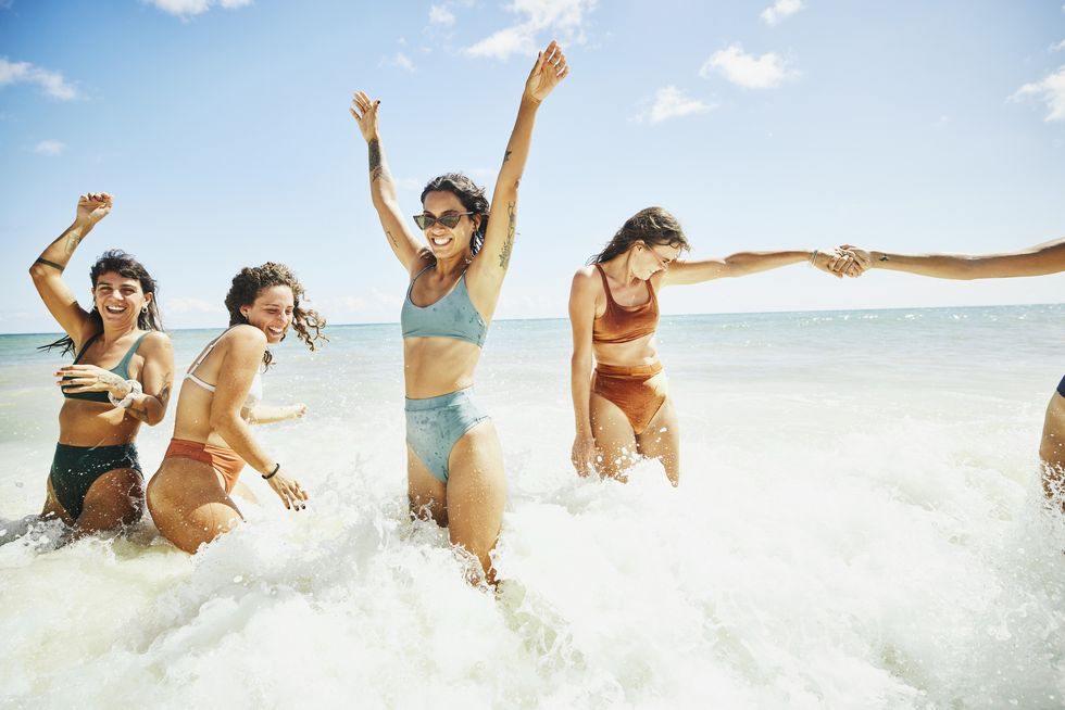 wide shot of laughing and smiling female friends playing in surf at tropical beach