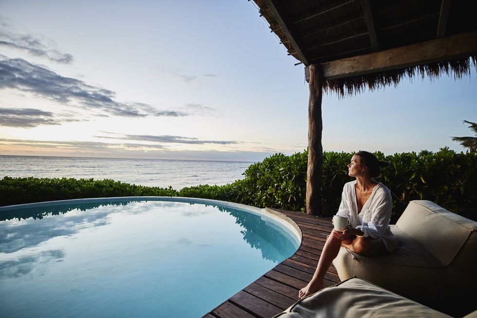 wide shot of woman enjoying sunrise next to pool at luxury suite at tropical resort