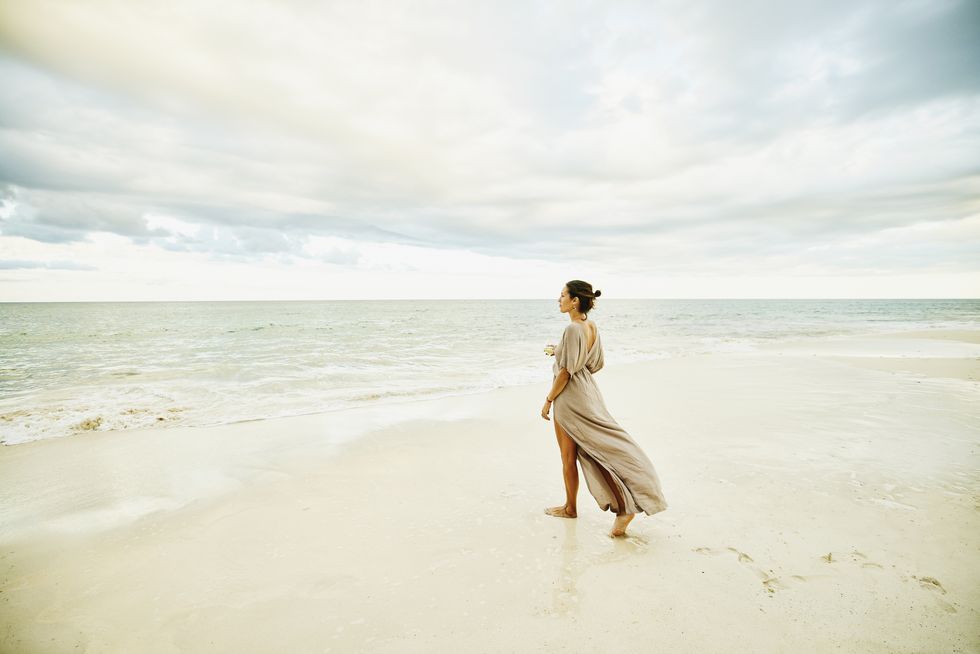 wide shot of woman walking on beach and enjoying sunset at tropical resort