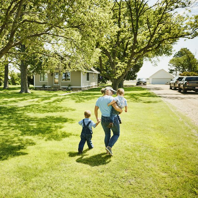 wide shot rear view of grandmother walking with grandsons through front yard of home