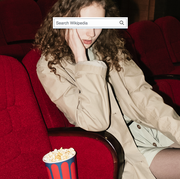 girl sitting in an empty movie theater next to a bucket of popcorn with a wikipedia search bar covering her eyes