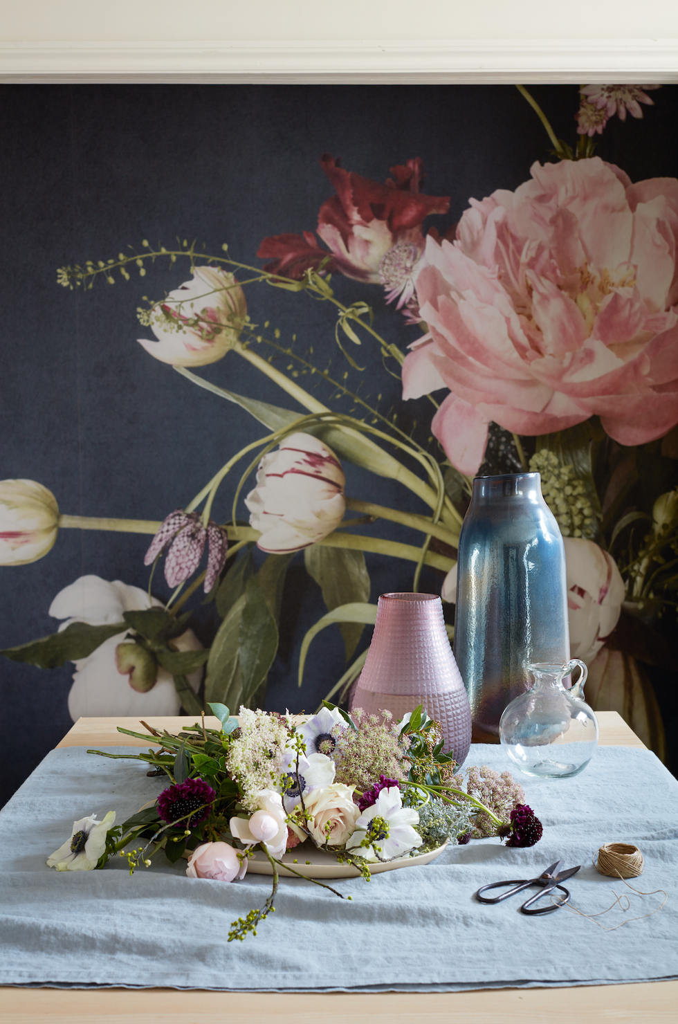 table with a white tablecloth and a bowl of cut flowers floral wallpaperin full bloomevoking the charm of a classic still life, an abundant bouquet of white and blush pink blooms sings out against a dark background