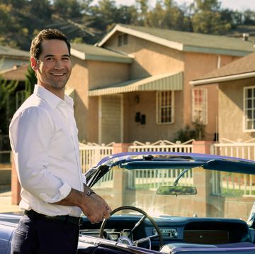 manuel garcia rulfo as mickey haller in lincoln lawyer season 2 smiling as he stands beside vintage blue lincoln convertible