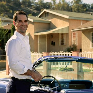 manuel garcia rulfo as mickey haller in lincoln lawyer season 2 smiling as he stands beside vintage blue lincoln convertible