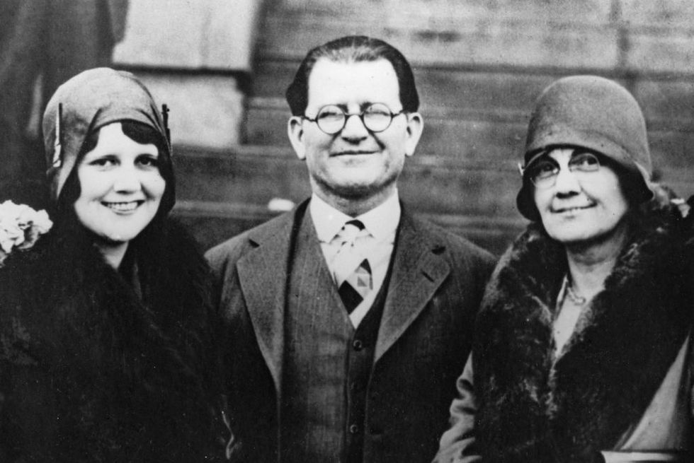 a black and white photo of william hale, wearing a suit and tie, smiling at the camera while standing next to two women