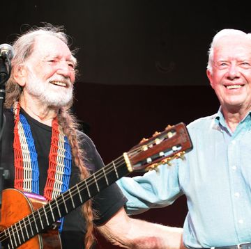 willie nelson holding a guitar and standing in front of a microphone while smiling and stnading next to a smiling jimmy carter