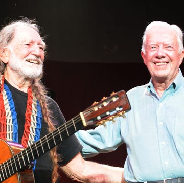 willie nelson holding a guitar and standing in front of a microphone while smiling and stnading next to a smiling jimmy carter