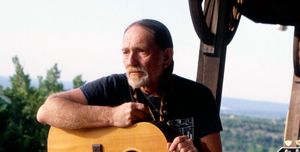willie nelson standing against a fence and holding a guitar