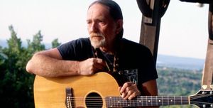 willie nelson standing against a fence and holding a guitar
