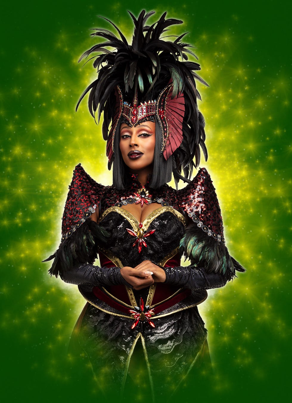 A person dressed in a dramatic costume with feathers and sequins surrounded by a vibrant green background