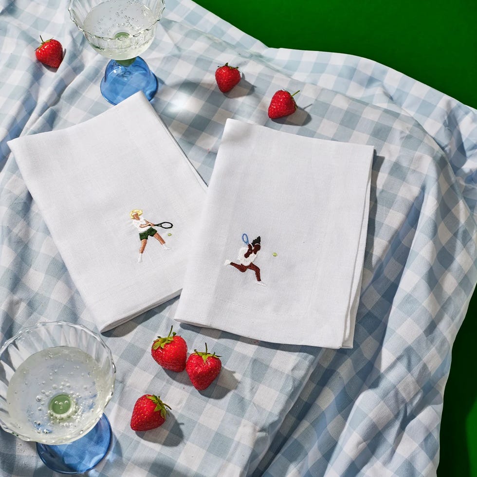 embroidered tennis themed napkins on a checkered tablecloth with strawberries and a glass of sparkling drink