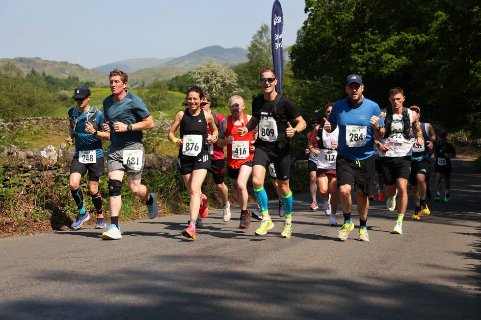 a group of people running on a road with hills in the background