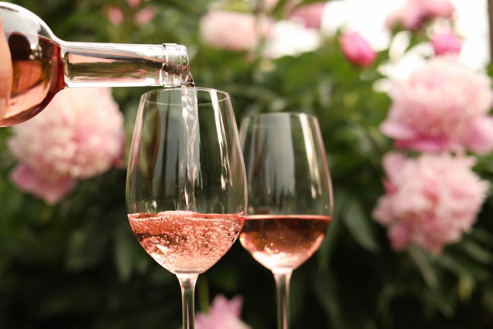 pouring rose wine from bottle into glass with flowers in the background