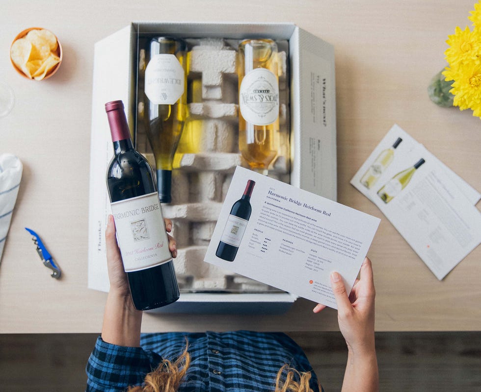 top down view of a woman holding a bottle of red wine and a tasting menu above a firstleaf delivery box