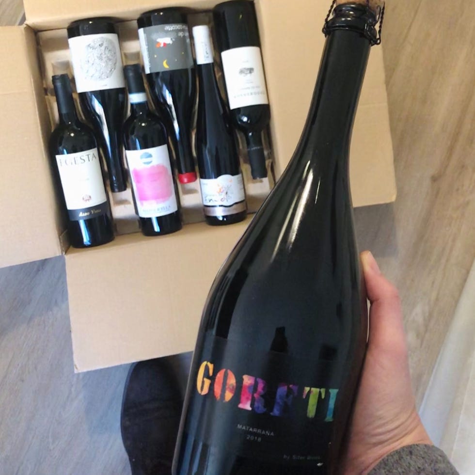 a hand holding a bottle of wine above a cardboard box with other wines