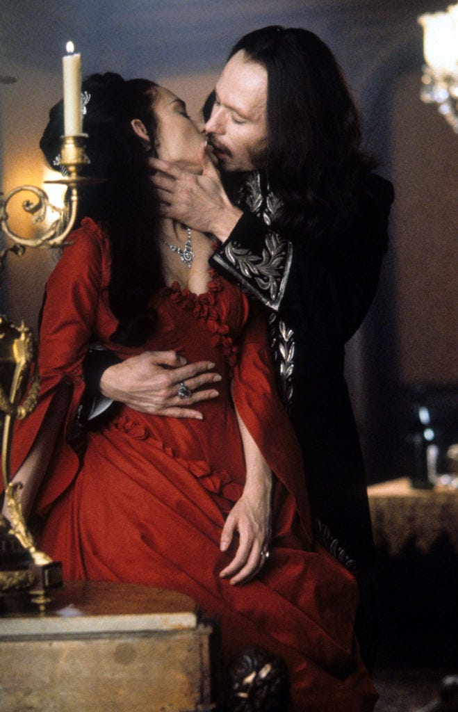 a promotional still from the movie dracula 2000 featuring gary oldman, wearing black, kissing winona ryder, who wears a red dress