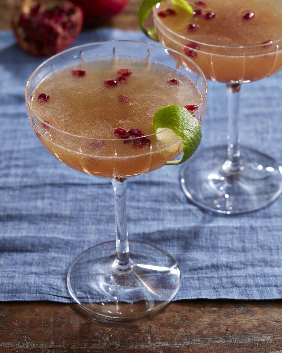 pomegranate french 75 in glasses with fresh pomegranate seeds and strips of lime peel as garnish