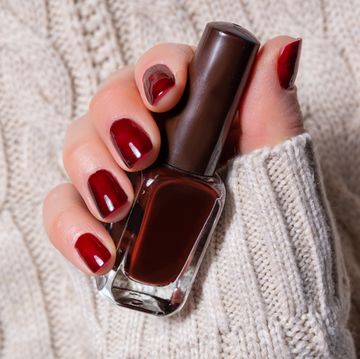 beautiful young woman hand with brown nails polish holding the small bottle with color for a manicure woman hand on white woolen sweater background manicure and beauty concept close up, selective focus fashion and femininity image