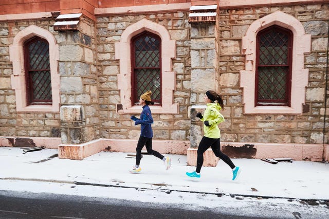 two individuals jogging along a snowcovered street beside a stone building