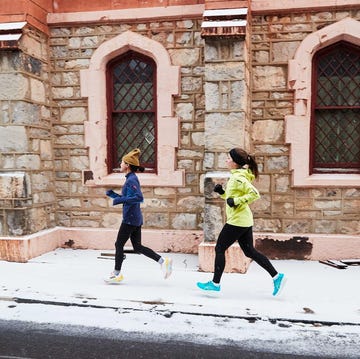 two individuals jogging along a snowcovered street beside a stone building two individuals jogging along a snowcovered street beside a stone building