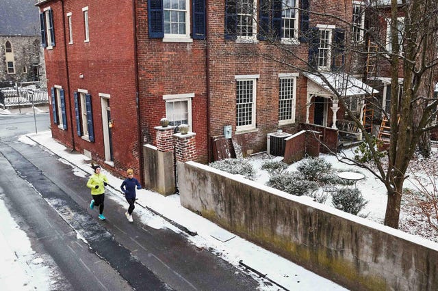 two individuals jogging on a snowcovered street alongside brick buildings