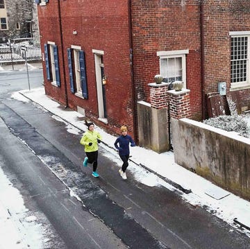 Two individuals jogging on a snowcovered street alongside brick buildings two individuals jogging on a snowcovered street alongside brick buildings