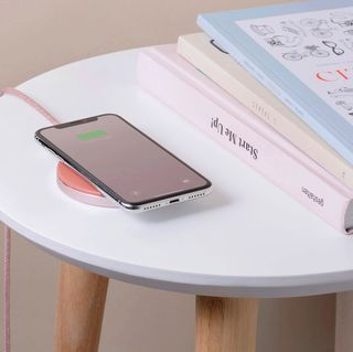 phone resting on native union wireless charger on side table with books