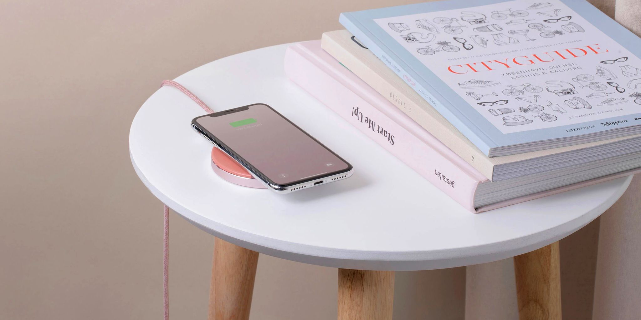 phone resting on native union wireless charger on side table with books