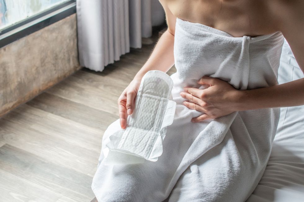 woman in towel folds open a sanitary pad as she sits on bed