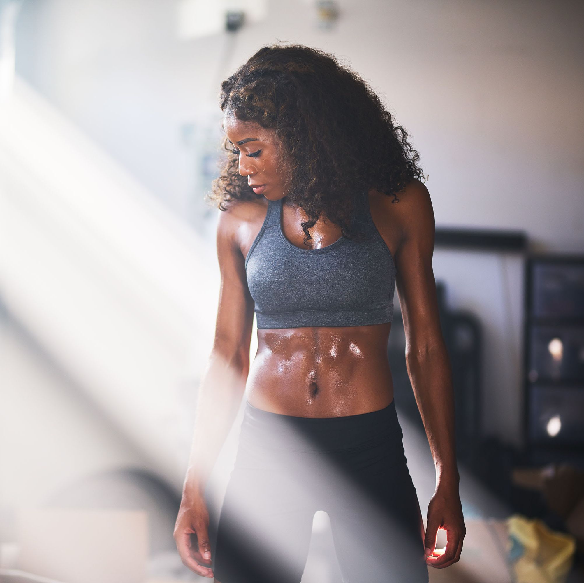 muscular african american woman sweating from work out in home gym with light rays
