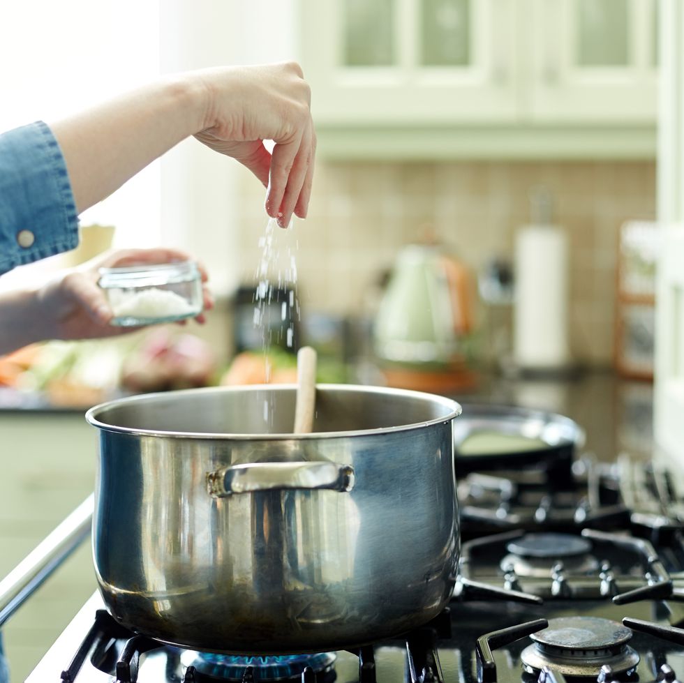 Woman adding salt to cooking pot on stove