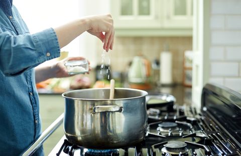 Woman adding salt to cooking pot on stove