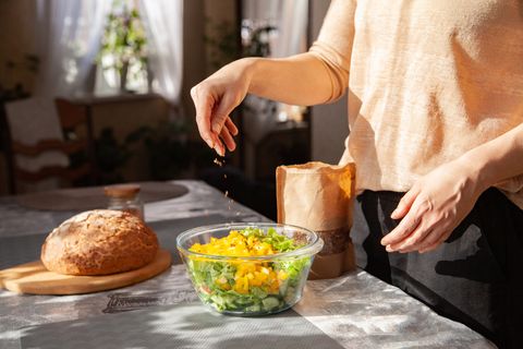 woman adding seeds to salad in bowl